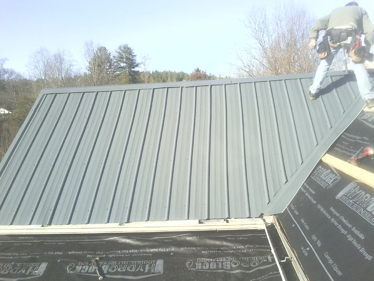 Crew installing dark green standing seam panels over synthetic underlayment in Mayer
