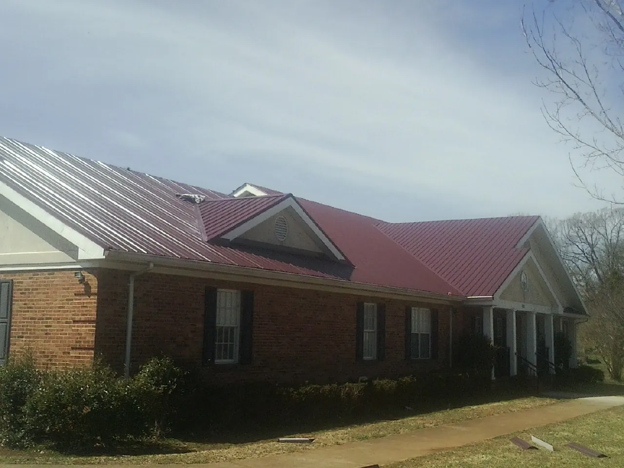 Red metal roof with gabled entries on a long brick building, from a Hail Damage Roof Repair job in Mayer