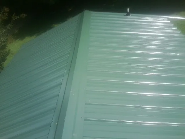 New green metal panels meeting at the ridge of a roof — Flat Roof Repair work by our crew in Mayer